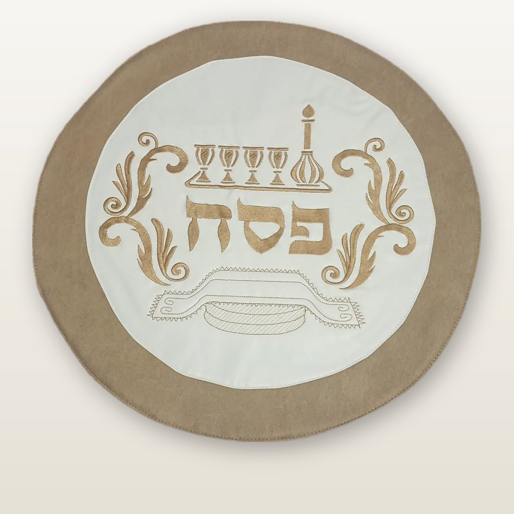 כיסוי מצה עגול בשמנת וחום, רקמת זהב של ארבע כוסות, קנקן ומצות סביב המילה פסח
