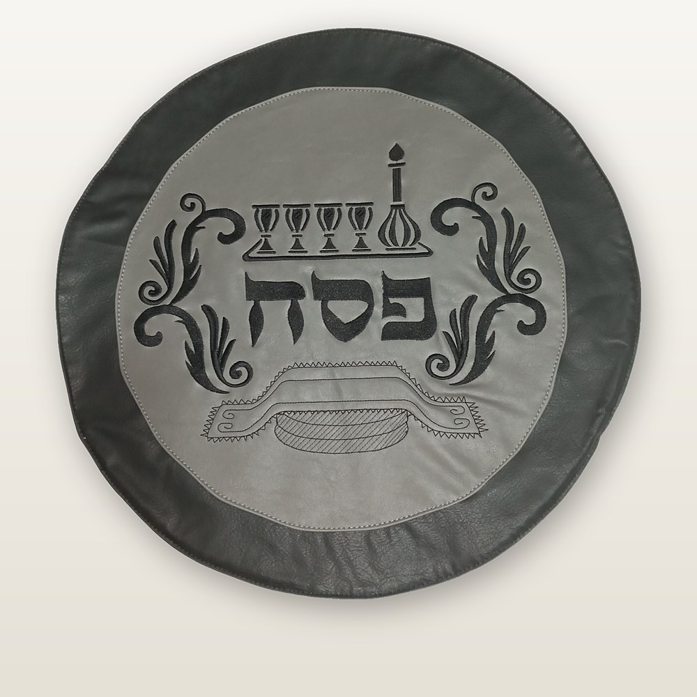 כיסוי מצה עגול מעור ארגנטינאי משובח, מרכז אפור בהיר ושוליים כהים, רקמה שחורה של ארבע כוסות ומצות