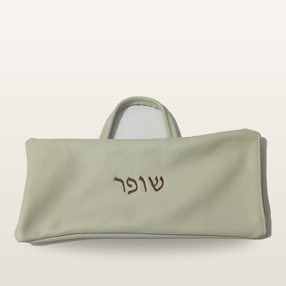 נרתיק לשופר מעור בגוון קרם עם ידית נשיאה, ועליו רקמת המילה שופר בגוון ערמון